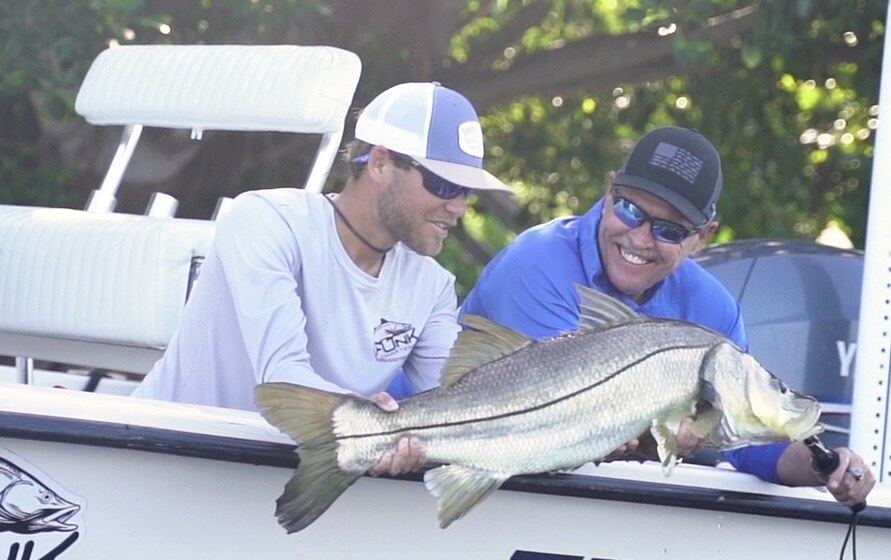 Captain Austin Funk holding a snook with a customer aboard the boat